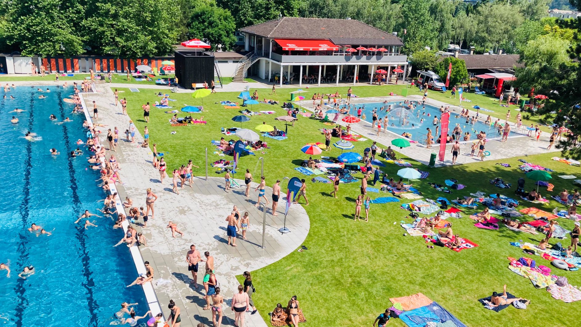 Das Hauptbecken und das Kinderbecken mit vielen Besuchern an einem sonnigen Tag