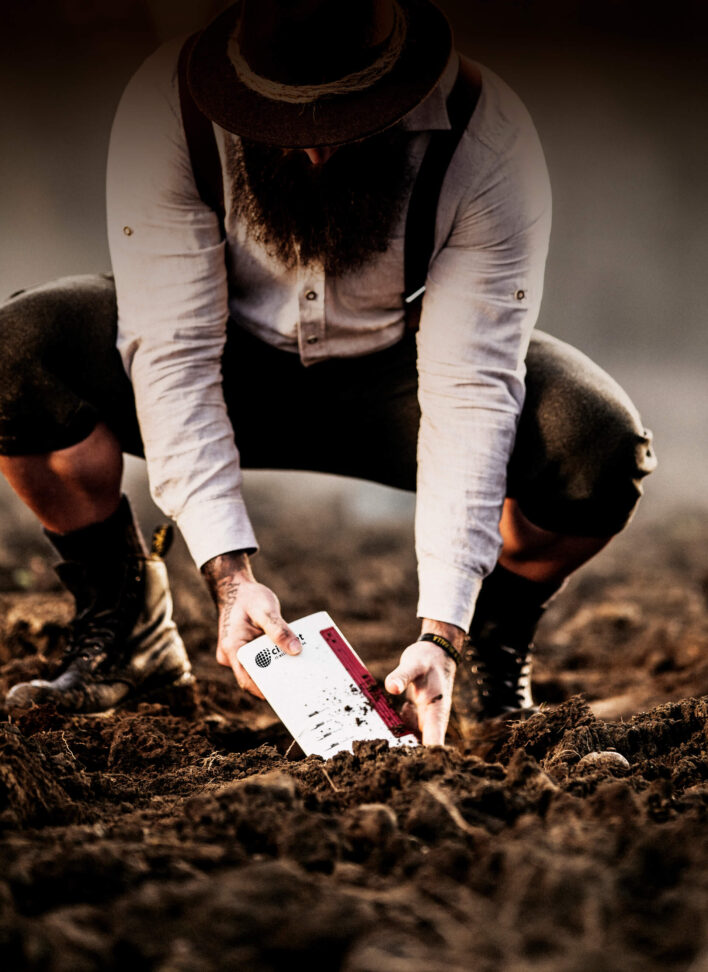 Ein bärtiger Mann mit Hemd, Hut und Lederhose kniet in der Erde, in den Händen hält er ein Citynet Modem