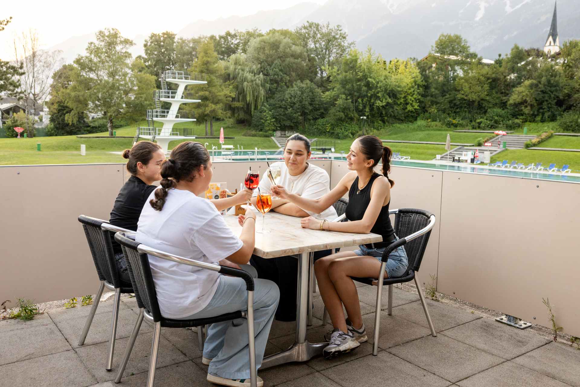 4 Damen genießen Cocktails im Restaurant mit Blick auf den Sprungturm