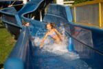 Zwei Mädchen rutschen lachend die blaue Wasserrutsche im Freien hinunter