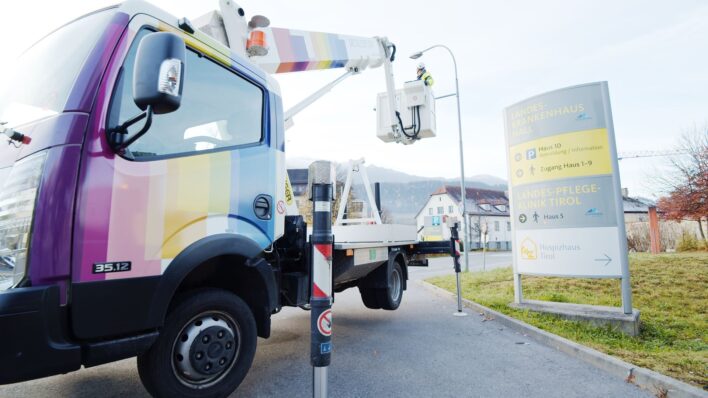 Hebebühnenfahrzeug mit bunter Hall AG Lackierung steht neben einem Schild vor einem Gebäude