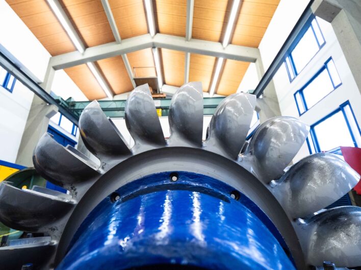 Nahaufnahme eines großen, silbernen Turbinenrads in einer Industriehalle mit Holzbalkendecke