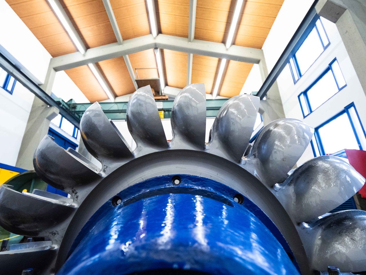 Nahaufnahme eines großen, silbernen Turbinenrads in einer Industriehalle mit Holzbalkendecke