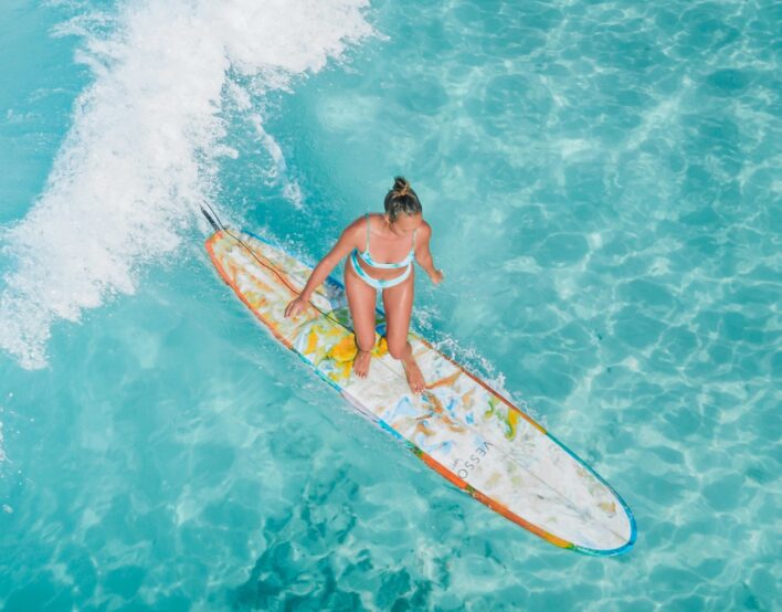 Frau im Bikini steht auf einem Surfbrett im türkisfarbenen Wasser