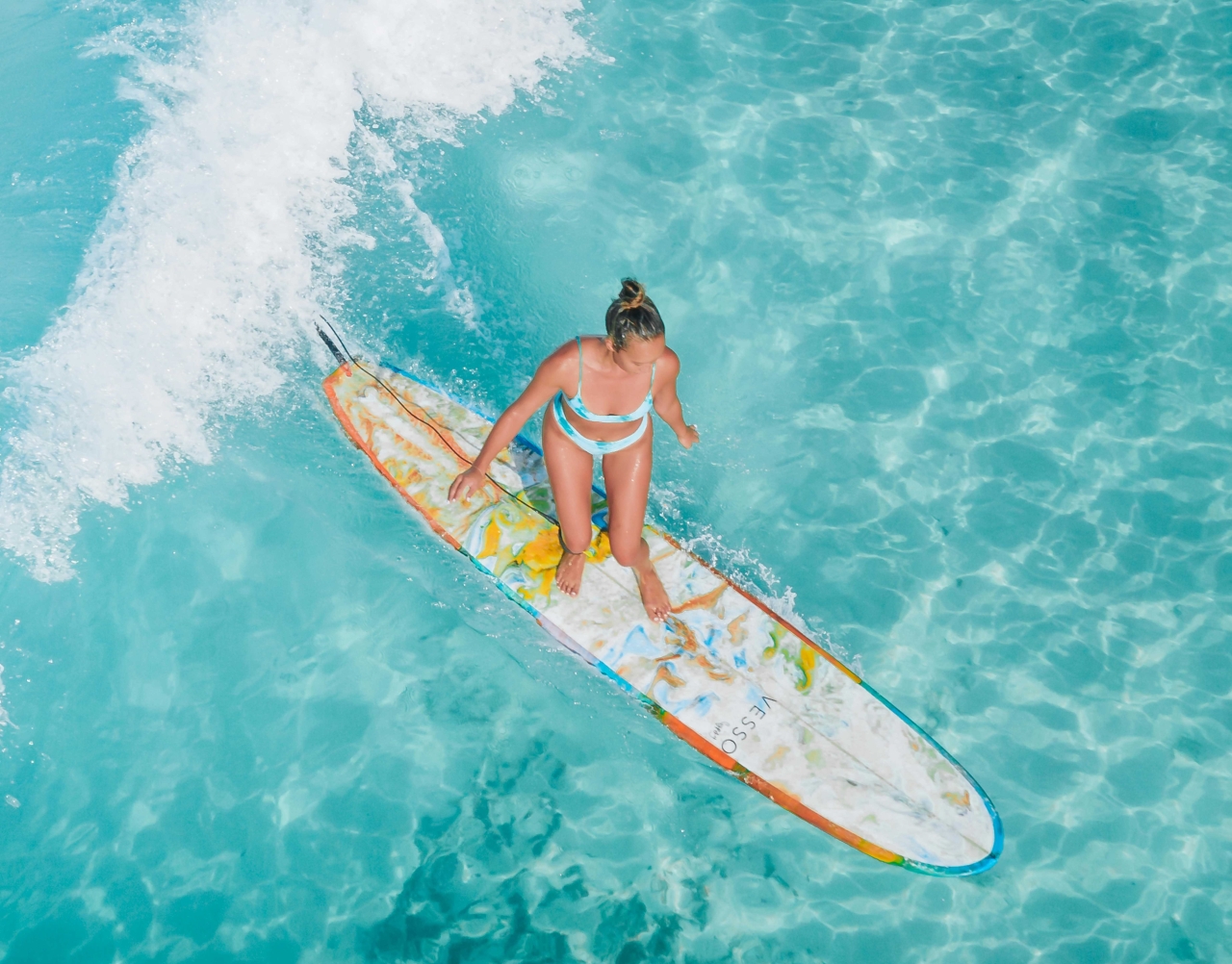 Frau im Bikini steht auf einem Surfbrett im türkisfarbenen Wasser