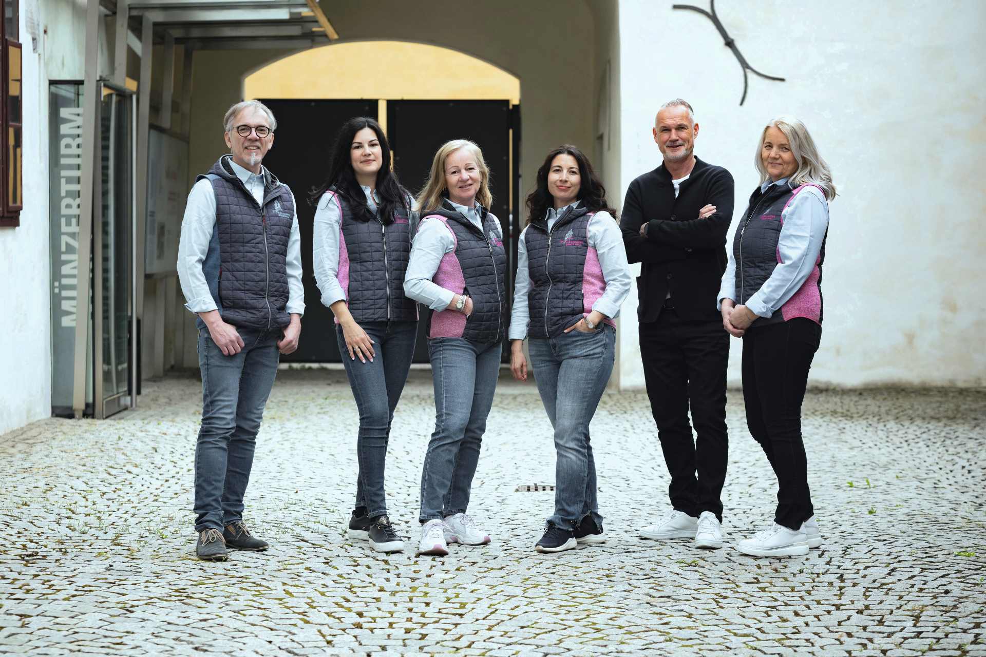 Sechs Personen stehen auf einem gepflasterten Hof vor einem Gebäude mit der Aufschrift 'Münzerturm'