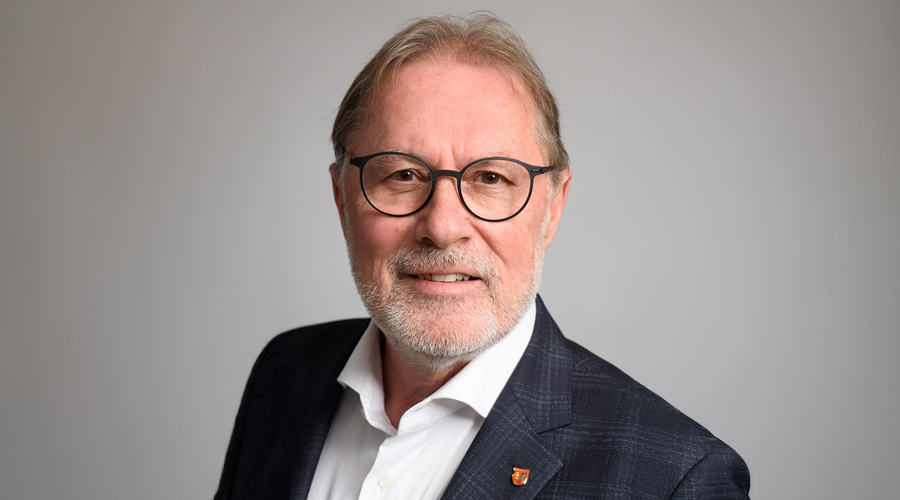 Porträt von Christian Margreiter, Bürgermeister von Hall in Tirol, in einem dunklen Sakko mit Brille vor einem neutralen Hintergrund.