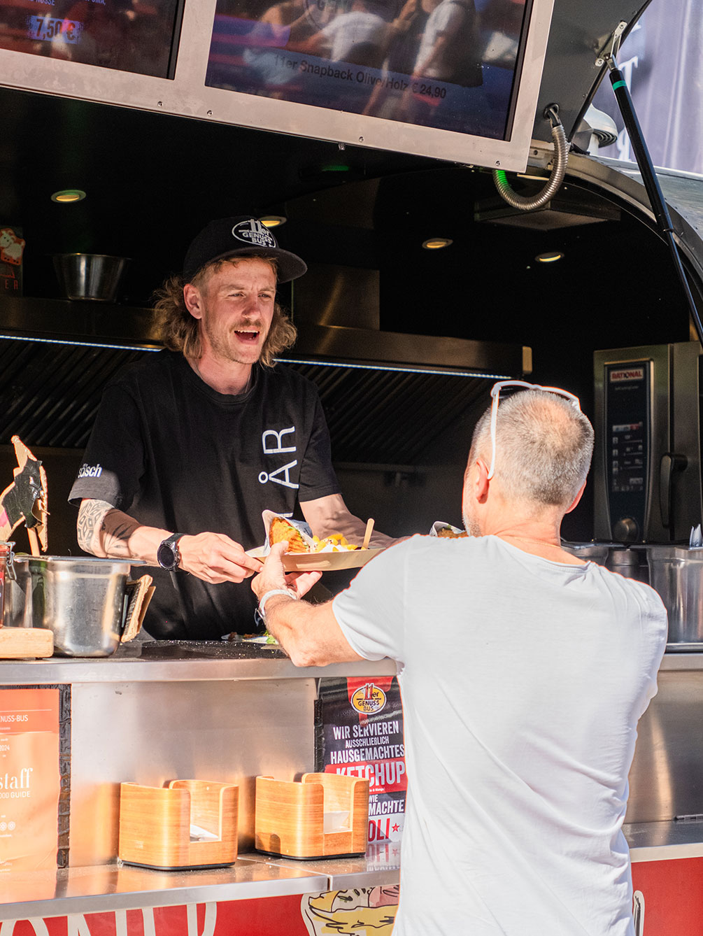 Ein freundlicher Mitarbeiter eines Food-Trucks reicht einem Besucher beim IATF in Innsbruck einen Teller mit frischem Essen.