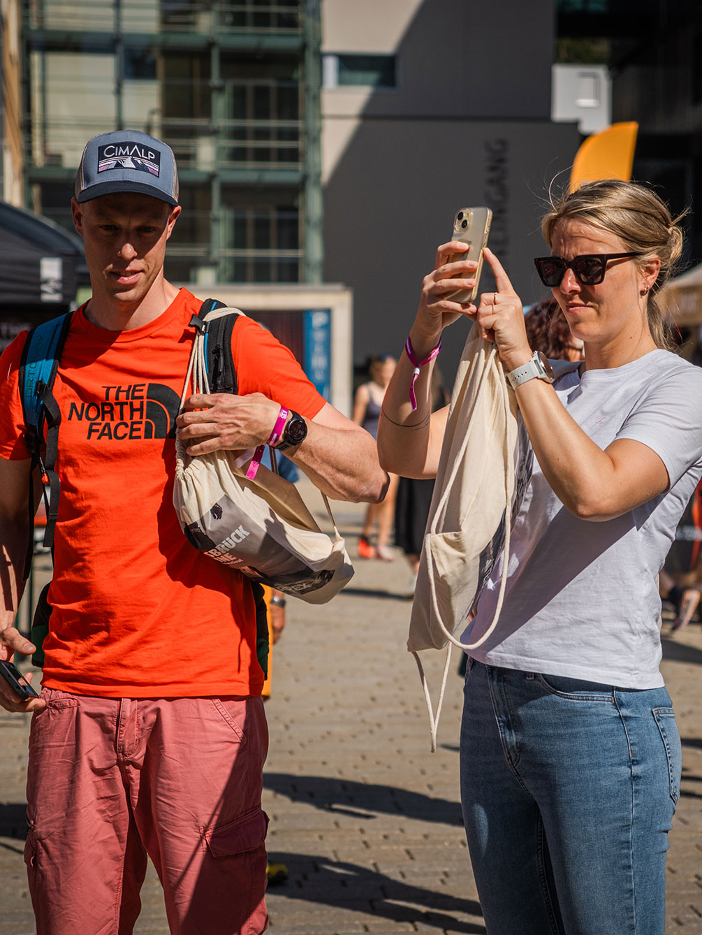 Zwei junge Besucher beim IATF in Innsbruck; ein Mann im orangefarbenen Shirt mit Starterbeutel und eine Frau, die mit ihrem Smartphone ein Foto macht.