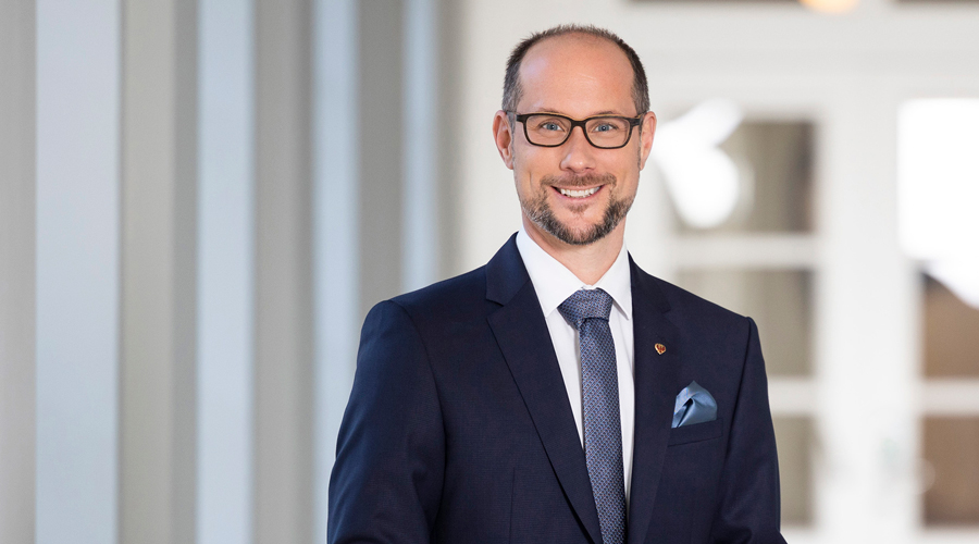 Porträt von Mario Gerber, Landesrat für Tourismus in Tirol, in einem dunklen Sakko mit blauem Einstecktuch und Brille.