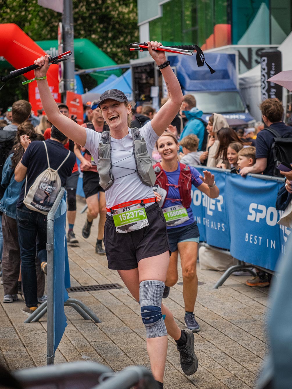Eine glückliche Trailrunnerin reißt beim Zieleinlauf des IATF in Innsbruck jubelnd die Laufstöcke in die Höhe.