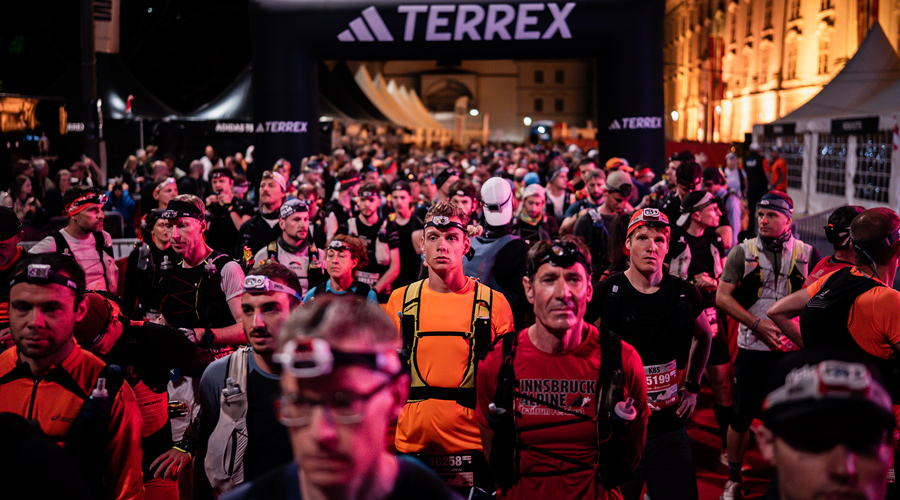 Eine große Gruppe von Läufern mit leuchtenden Stirnlampen steht nachts im Startbereich unter einem schwarzen adidas TERREX Bogen in Innsbruck.