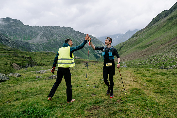 Ein Trailrunner gibt einem Streckenposten in einer gelben Warnweste ein High-Five auf einem alpinen Pfad während des Innsbruck Alpine Trailrun Festivals.