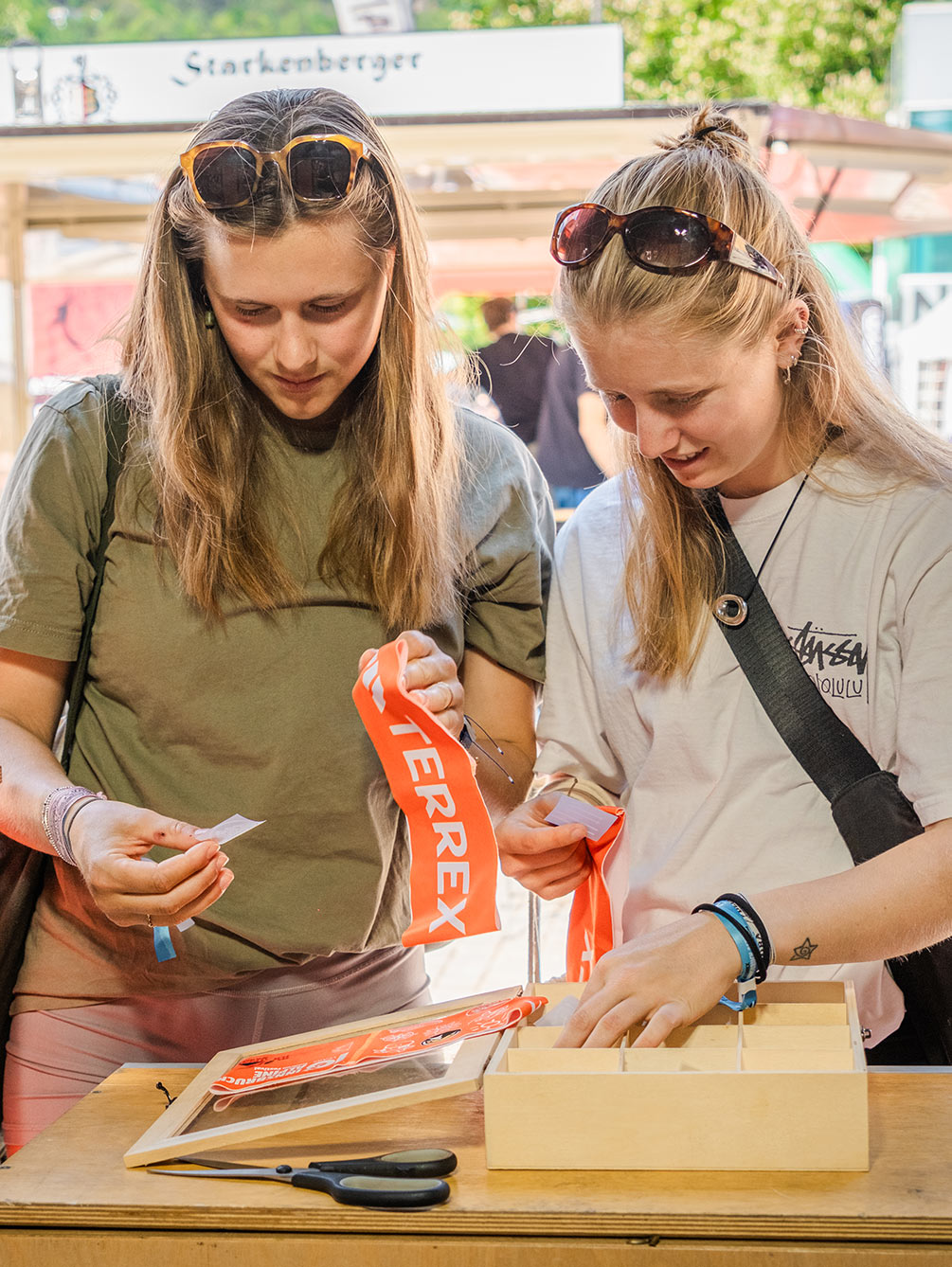 Zwei junge Frauen begutachten orangefarbene Adidas Terrex Startbänder an einem Holztisch während des Innsbruck Alpine Trailrun Festivals.