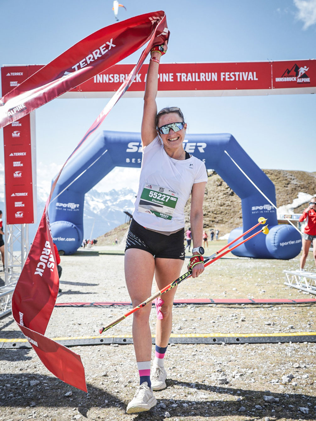 Eine glückliche Trailrunnerin hebt im Ziel des Innsbruck Alpine Trailrun Festivals triumphierend das rote Finisher-Band in die Höhe.
