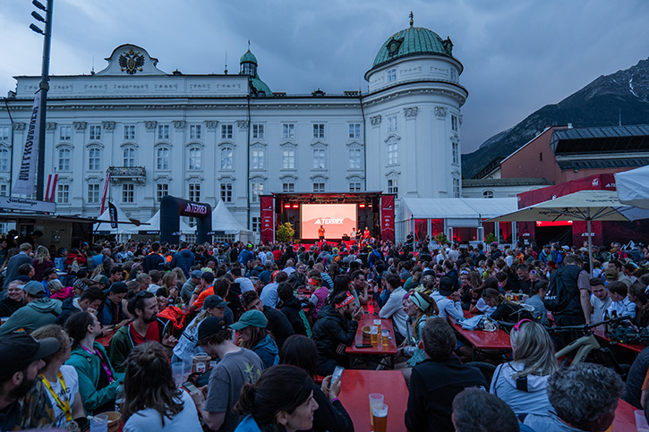 Abendliche Event-Area des Innsbruck Alpine Trailrun Festivals vor der beleuchteten Hofburg mit Publikum an Biertischen und einer großen Bühne mit Terrex-Logo.