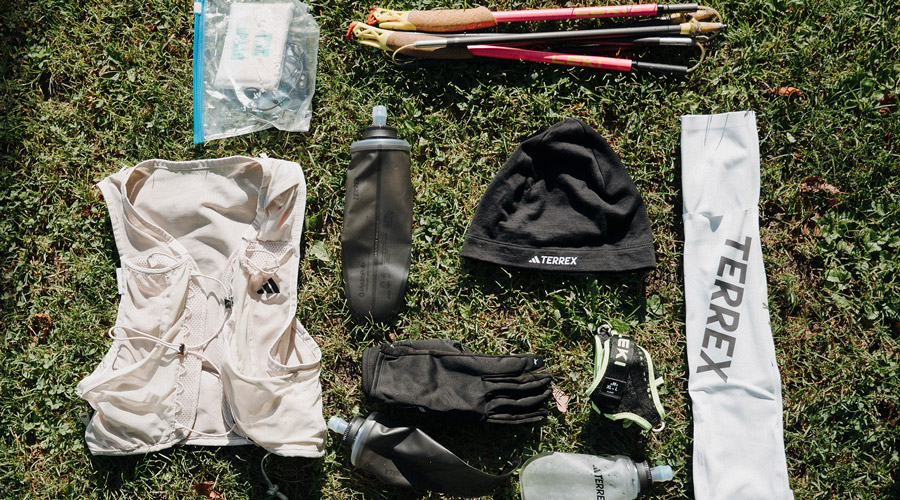 Professionelles Trailrunning-Equipment inklusive Laufweste, Trinkflaschen, Stöcken und Bekleidung von Adidas TERREX flach auf Gras ausgebreitet für das IATF.