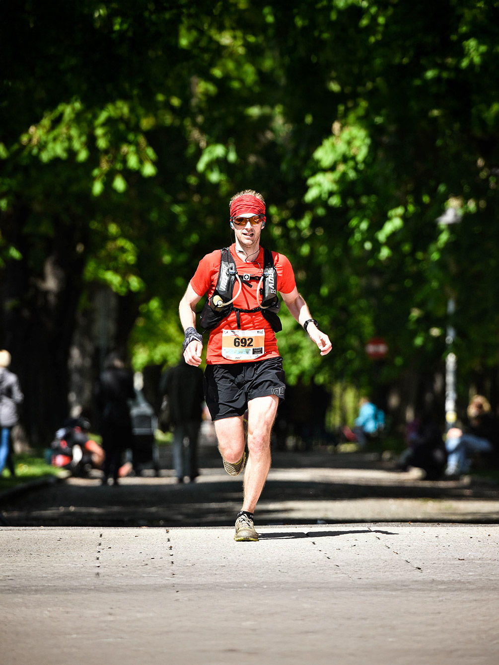 Ein Trailrunner mit rotem Shirt und rotem Stirnband läuft während des Innsbruck Alpine Trailrun Festivals konzentriert durch eine schattige Baumallee.
