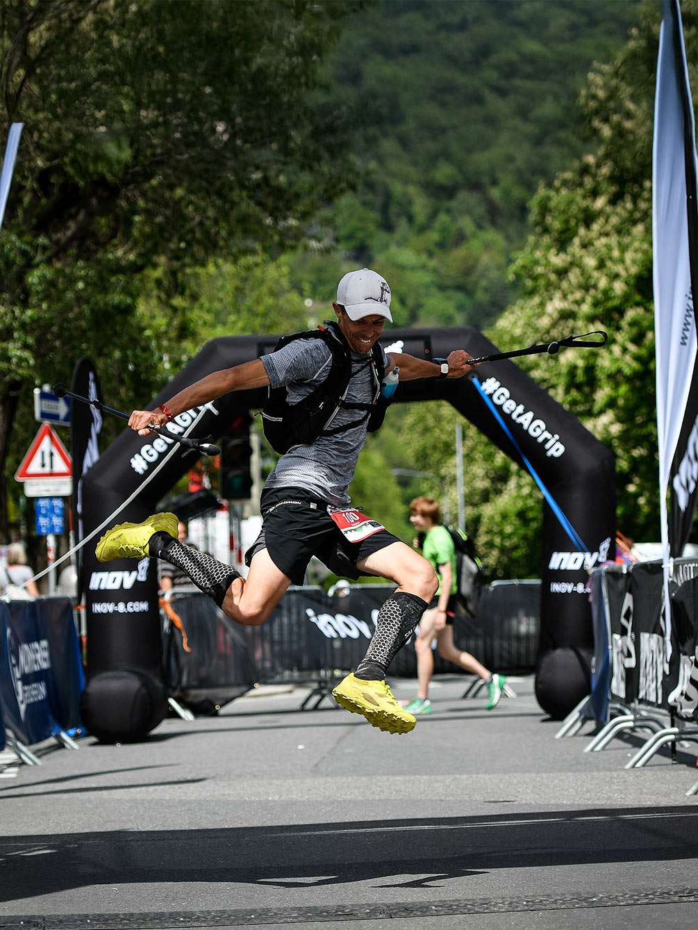 Ein Trailrunner springt mit ausgebreiteten Armen und Laufstöcken voller Freude über die Ziellinie des Innsbruck Alpine Trailrun Festivals.