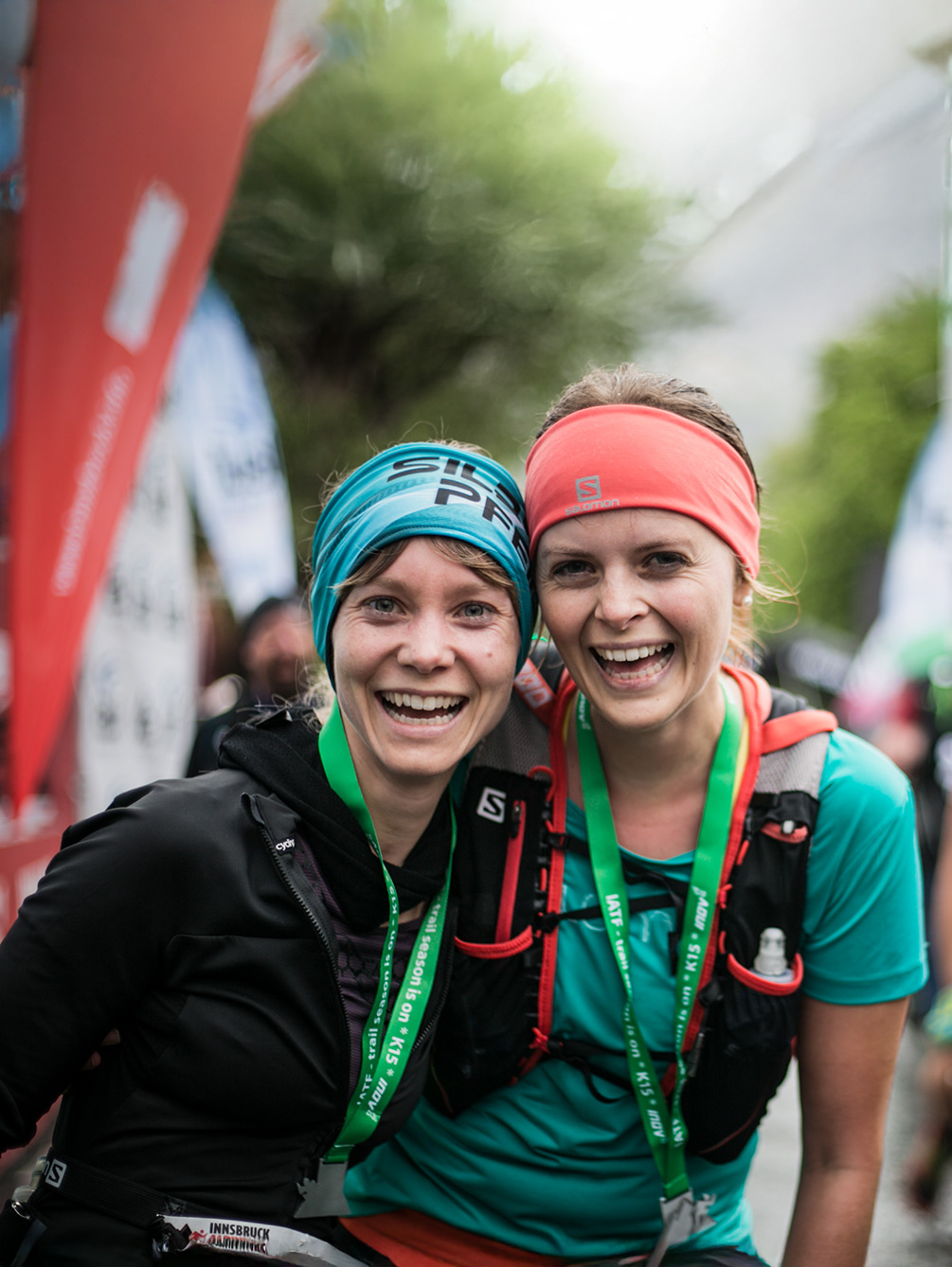 Zwei lachende Trailrunnerinnen mit Stirnbändern und Finisher-Medaillen nach dem Lauf beim Innsbruck Alpine Trailrun Festival.