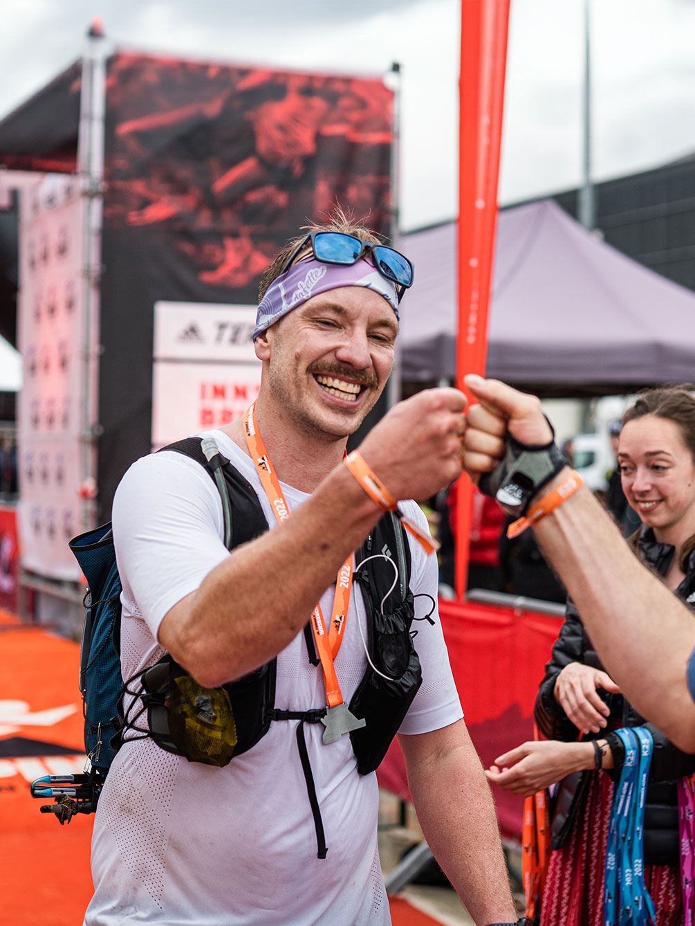 Ein lachender Trailrunner feiert seinen Erfolg beim Innsbruck Alpine Trailrun Festival mit einem freundschaftlichen "Fist Bump" im Zielbereich.