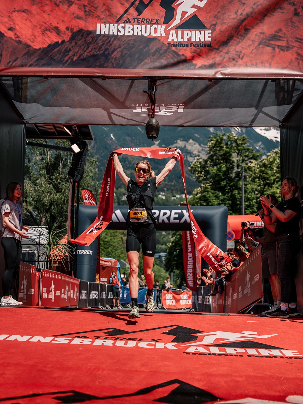 Eine strahlende Läuferin reißt beim Zieleinlauf des Innsbruck Alpine Trailrun Festivals das rote Siegerband in die Höhe.