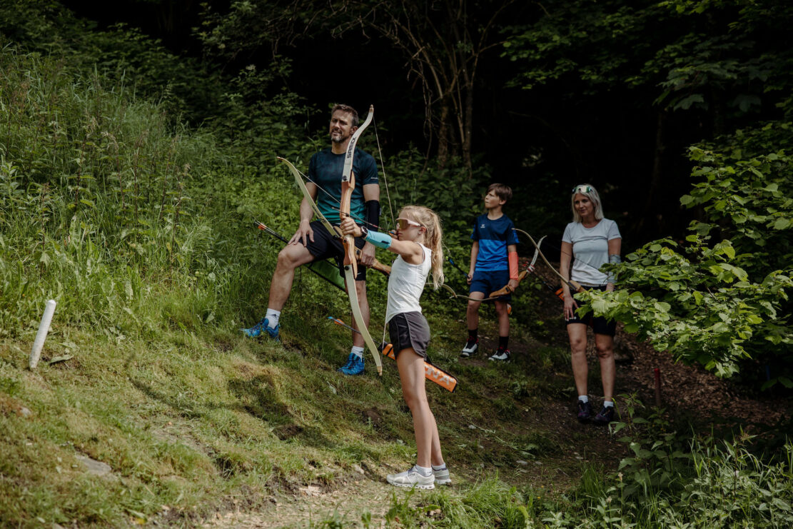 EIne Familie hat Spass beim Bogenschiessen im Alpendorf waehrend ihres Sporturlaubs im Alpina.