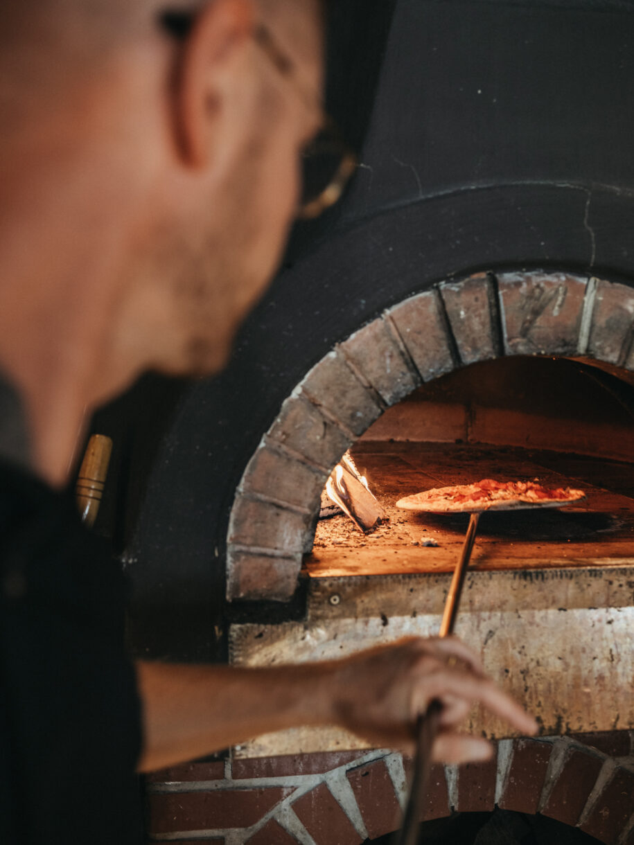Pizzakoch beim backen einer Holzofen Pizza im BistrO Alpendorf - Alpina Alpendorf